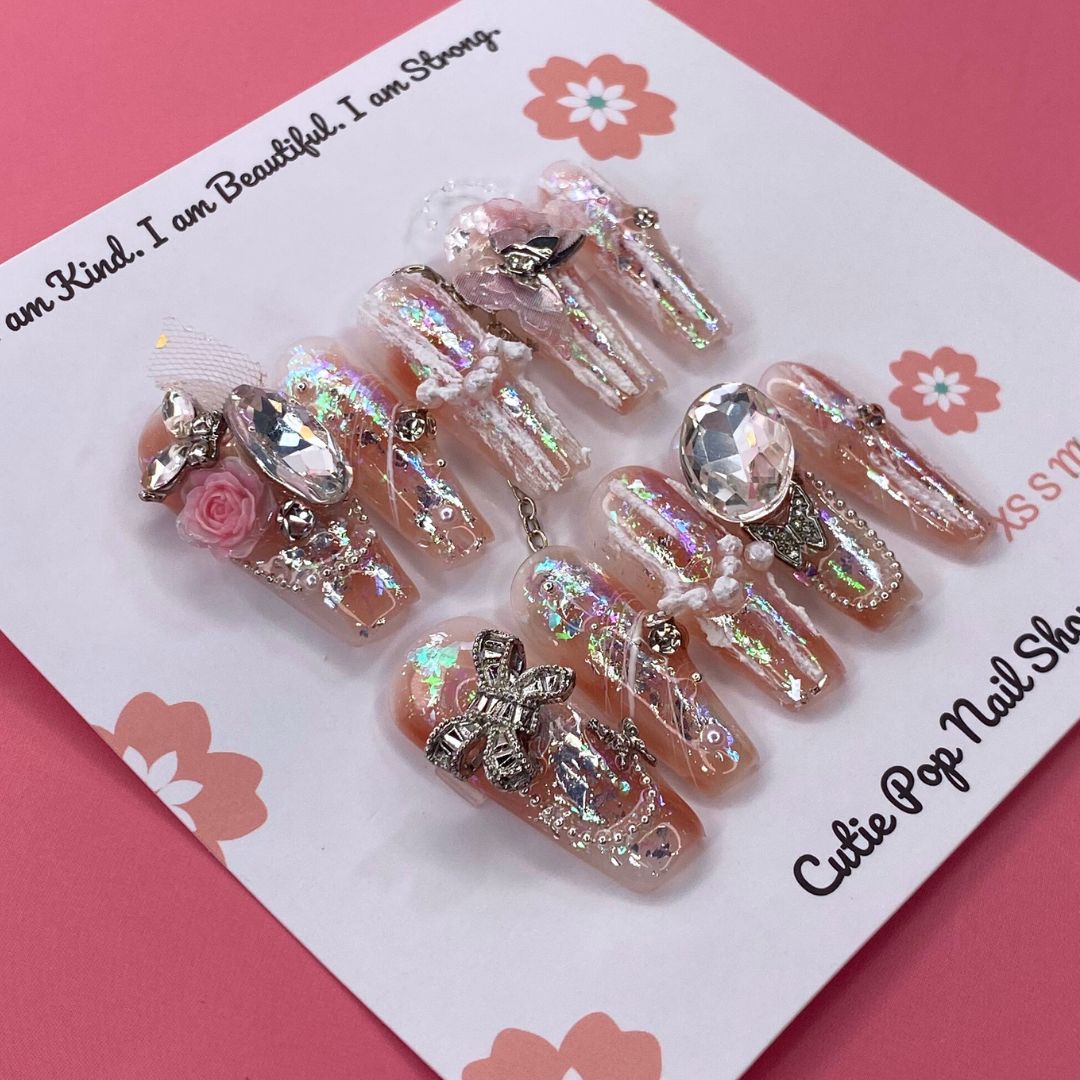 Bougie Bling 19 press on nails by CutiePop Nail Shop showcasing long coffin shaped nails with a luxe metallic rose gold base, oversized 3D gem clusters, sparkling rhinestone accents, and hand sculpted detailing—offering a glamorous, high end aesthetic.

