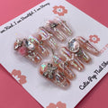 Bougie Bling 19 press on nails by CutiePop Nail Shop showcasing long coffin shaped nails with a luxe metallic rose gold base, oversized 3D gem clusters, sparkling rhinestone accents, and hand sculpted detailing—offering a glamorous, high end aesthetic.

