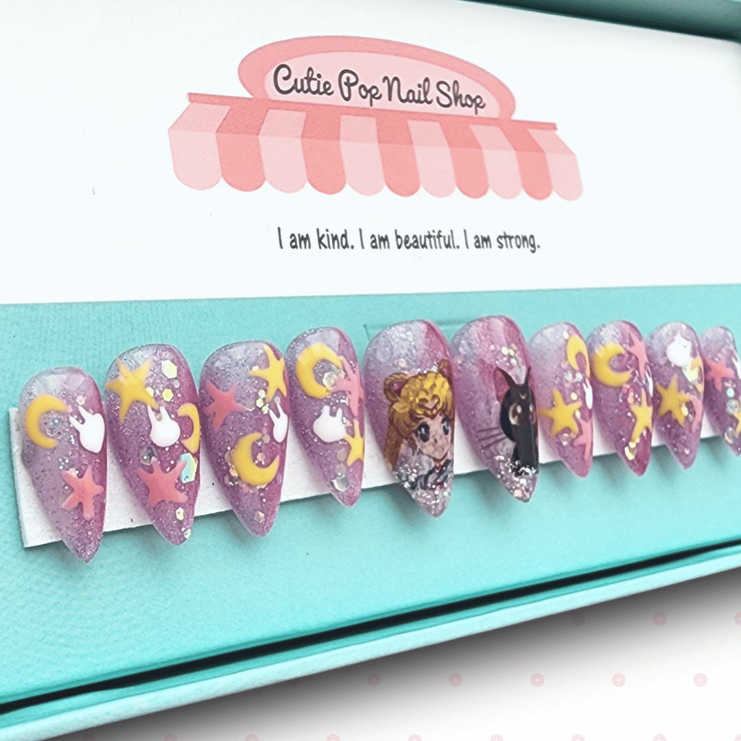 Kawaii Moon press‑on nails showcasing short- to medium-length almond-shaped or round nails in a soft pastel pink and lavender jelly base. Accented with hand-painted or high-detail 2D moon decals, iridescent star sequin glitter, and tiny metallic foil moons. Each nail glimmers in a dreamy glow—designed for a magical, kawaii-inspired manicure. (Kit includes ten reusable nails, adhesive tabs, a mini nail file, and cuticle stick.