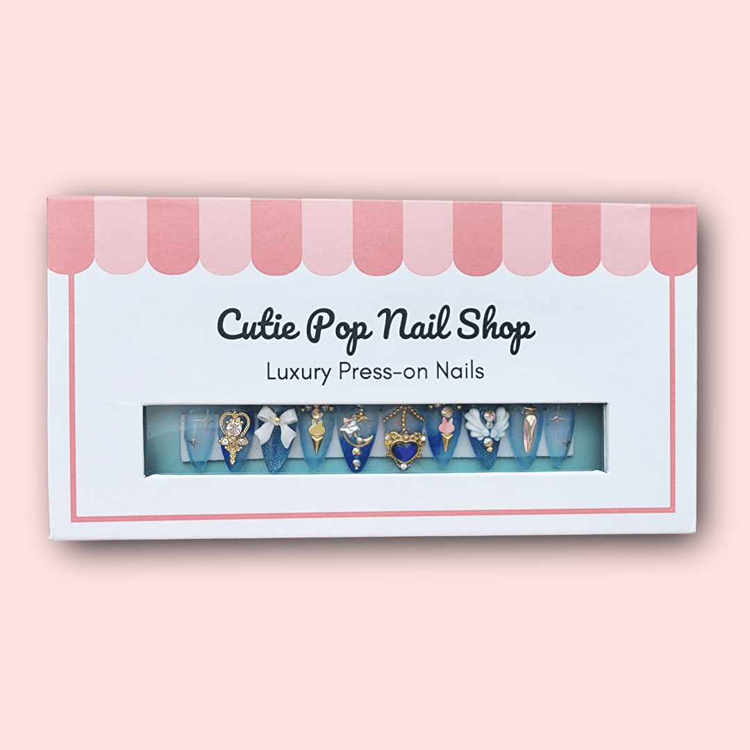 Mercury press on nails by CutiePop Nail Shop featuring medium stiletto shaped nails in pastel aqua blue and soft white tones. Several accent nails highlight hand painted chibi-style Princess Mercury illustrations, crescent moon decals, holo-flake glitter, and water droplet motifs. Finished with a glossy gel coat and metallic shimmer that capture Sailor Mercury’s graceful, aquatic elegance. The set includes 10 reusable handmade nails, jelly adhesive tabs, mini nail file, and cuticle stick.