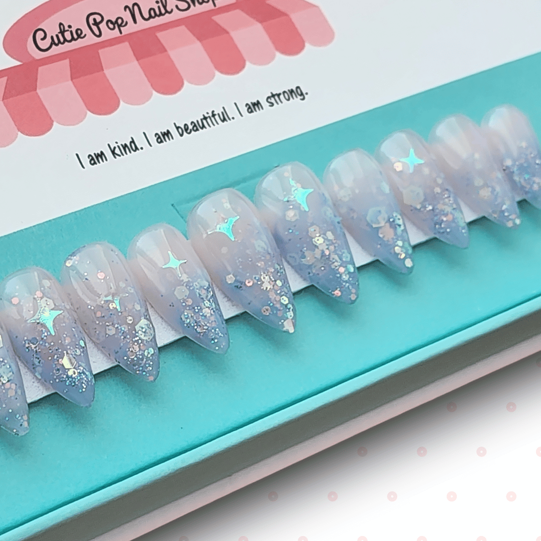Fantasy (Lavender) press‑on nails by CutiePop Nail Shop featuring short-to-medium length almond-, round-, or coffin-shaped nails coated in dreamy lavender syrup jelly gel polish. Each nail is sprinkled with holographic star sequin glitter for a celestial shimmer effect. The set includes ten handmade reusable nails, jelly adhesive tabs, a mini nail file, and a cuticle stick—offering a whimsical, fantasy-inspired manicure perfect for summer enchantment.