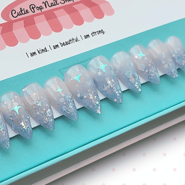 Fantasy (Lavender) press‑on nails by CutiePop Nail Shop featuring short-to-medium length almond-, round-, or coffin-shaped nails coated in dreamy lavender syrup jelly gel polish. Each nail is sprinkled with holographic star sequin glitter for a celestial shimmer effect. The set includes ten handmade reusable nails, jelly adhesive tabs, a mini nail file, and a cuticle stick—offering a whimsical, fantasy-inspired manicure perfect for summer enchantment.