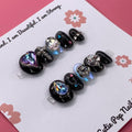 Cosmic Goth press on nails by CutiePop Nail Shop featuring medium round shaped nails in black and purple tones with celestial designs like stars and moons, accented with metallic or glittery finishes for a dark, dreamy aesthetic.

