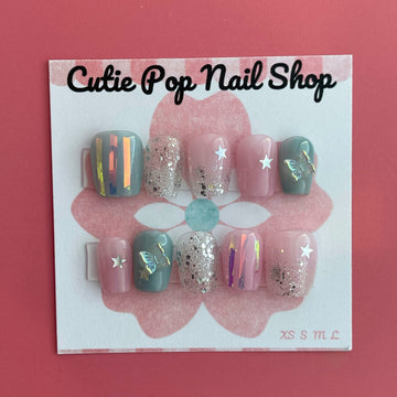 Dreamy Butterfly press‑on nails by CutiePop Nail Shop featuring coffin-shaped extra short nails in soft pastel pinks and blues, accented with hand-painted butterfly wing motifs, metallic foil shimmer, and delicate glitter sparkle. The set includes reusable press-on tabs, a mini nail file, and a cuticle stick—offering a fantasy-inspired, playful yet elegant manicure.