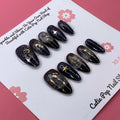 Galaxy Stars press on nails by CutiePop Nail Shop featuring medium almond shaped nails in deep navy and black tones, adorned with shimmering star, moon, and cosmic accents for a bold, celestial-inspired look.

