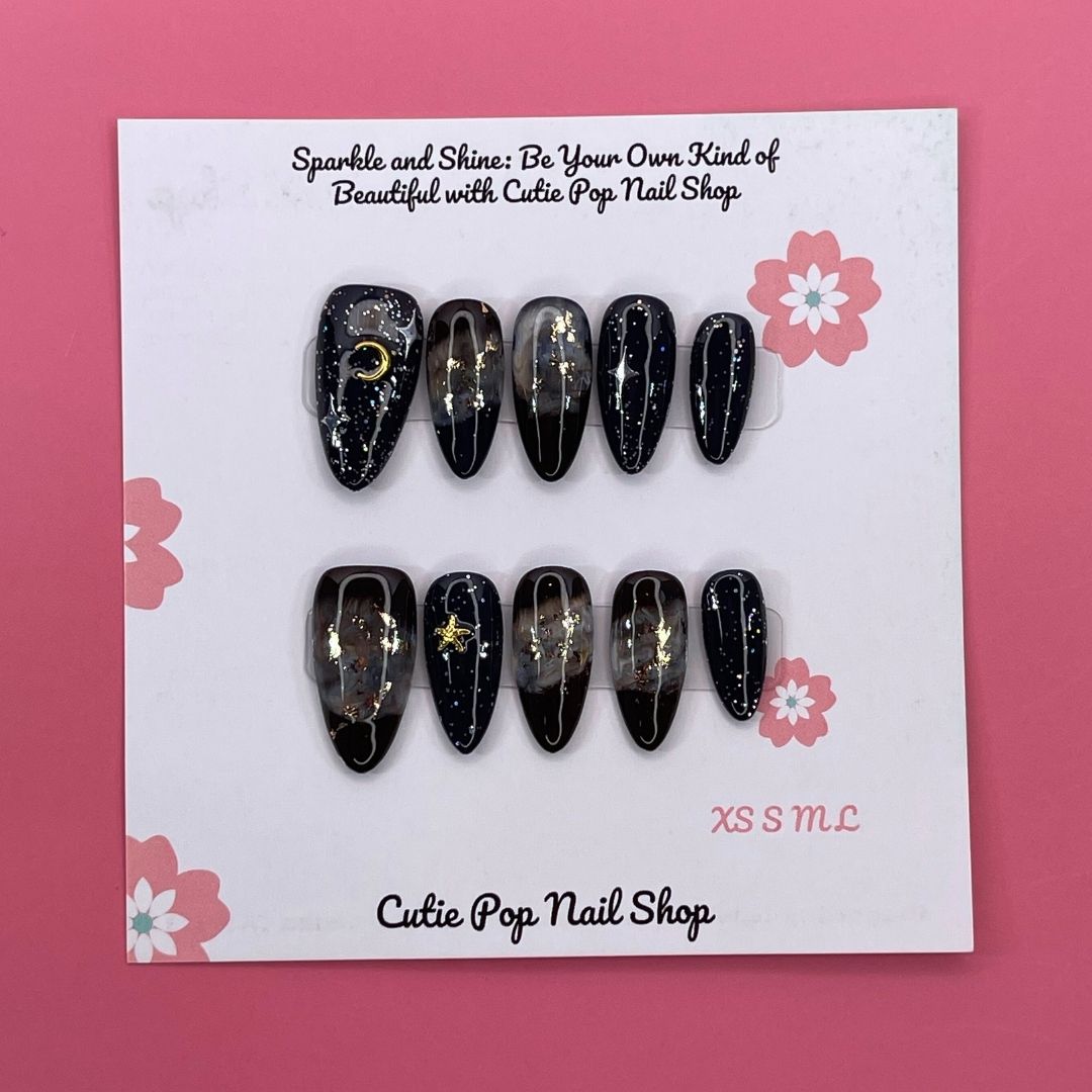 Galaxy Stars press on nails by CutiePop Nail Shop featuring medium almond shaped nails in deep navy and black tones, adorned with shimmering star, moon, and cosmic accents for a bold, celestial-inspired look.

