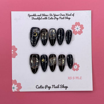 Galaxy Stars press on nails by CutiePop Nail Shop featuring medium almond shaped nails in deep navy and black tones, adorned with shimmering star, moon, and cosmic accents for a bold, celestial-inspired look.

