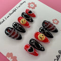 Stray Kids Concert-Inspired press on nails by CutiePop Nail Shop featuring medium almond shaped nails in bold red and black tones, adorned with heart charms, chains, and cartoon face accents. Designed for fans who want to rock a fierce, edgy look with playful K-pop flair.

