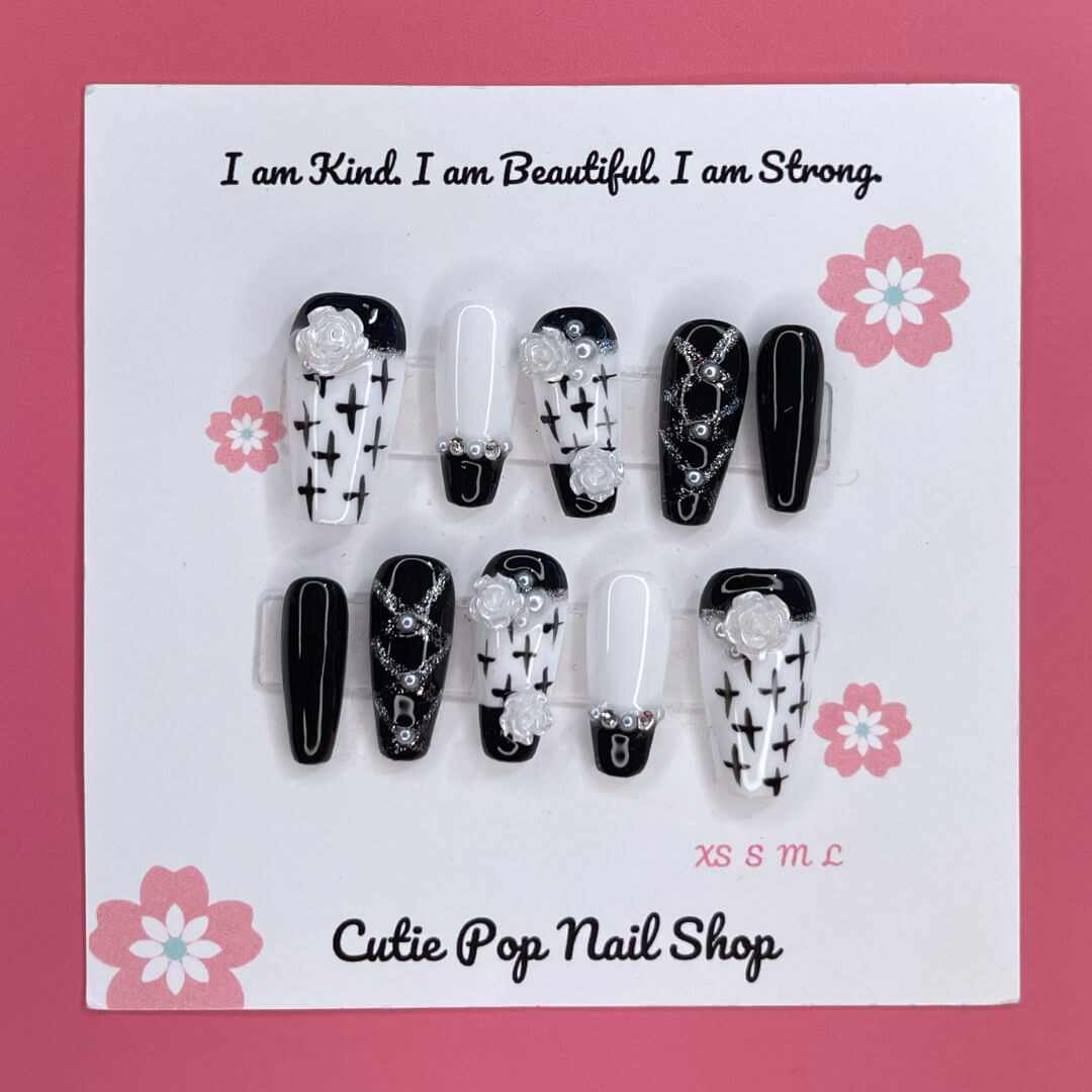 Floral Cross Monochrome press‑on nails by CutiePop Nail Shop featuring a chic coffin-shaped medium-length set in a classic black-and-white palette. Hand-painted white flowers and bold black crosses decorate alternating nails, accentuated by subtle metallic shimmer and glossy gel finish—creating a sophisticated gothic-inspired floral aesthetic.