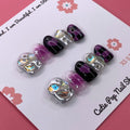 Galaxy Beauty press-on nails by CutiePop Nail Shop featuring extra short squoval-shaped nails in a cosmic blend of deep blue, purple, and black tones, accented with shimmering stars, moons, and glitter for a bold celestial look.

