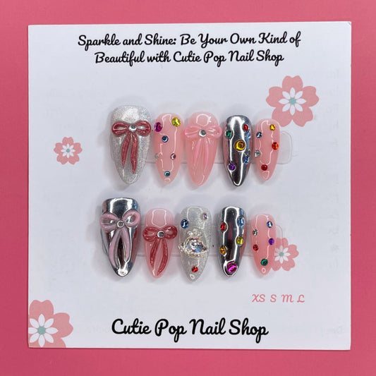 Gem Princess press-on nails by CutiePop Nail Shop featuring a creamy blush-pink base with ultra-fine shimmer, hand-placed pastel gem clusters, and clear rhinestones. Select nails are accented with tiny pearls or heart motifs for added charm. Crafted in a medium-length almond shape with a glossy gel finish, this design brings an elegant and whimsical princess-like aesthetic to your manicure. Each set includes 10 reusable handmade nails, jelly adhesive tabs, a mini nail file, and a cuticle stick for effortles