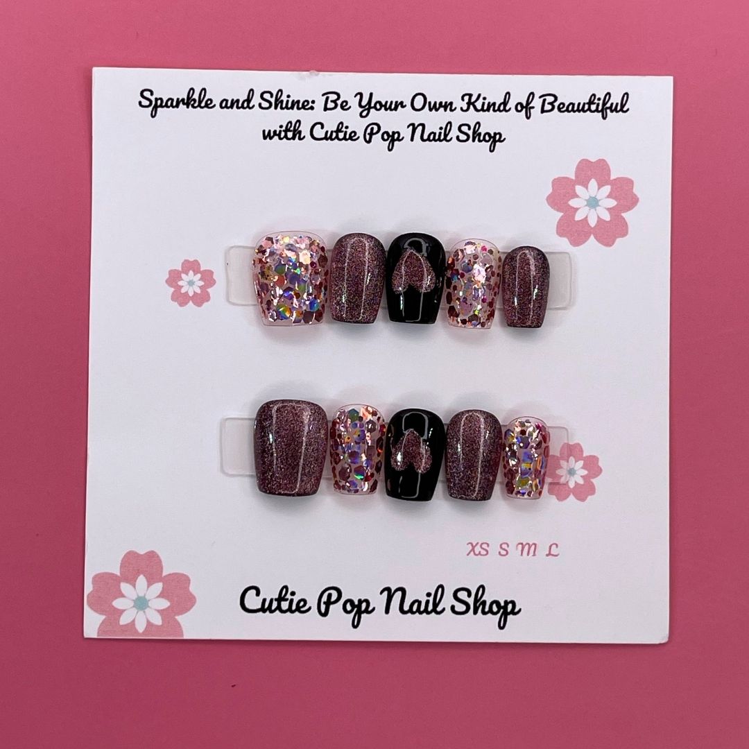 Glittered Heart press-on nails by CutiePop Nail Shop featuring short square-shaped nails in soft pink or nude tones, adorned with glitter accents and heart-shaped charms for a sweet and romantic finish.

