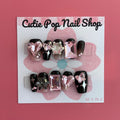 Gothic Girly press‑on nails by CutiePop Nail Shop featuring medium-length coffin-shaped nails painted in glossy black with alternating muted pink accent nails. Adorned with edgy gothic motifs—such as skulls, crosses, and mini bows—plus glittery accents and metallic studs, the design balances feminine charm with dark, rebellious elegance. The set arrives with reusable adhesive tabs, a mini nail file, and a cuticle stick for a complete application kit.