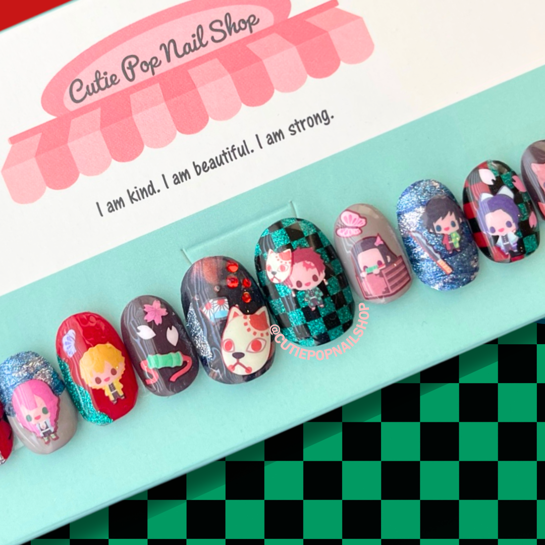 Slayer Nails press-on nails by CutiePop Nail Shop featuring medium-length round-shaped nails adorned with anime-inspired chibi character decals from the Demon Slayer universe. Each custom set is handcrafted and sized to fit your natural nails. Includes 10 reusable gel nails, jelly adhesive tabs, a mini nail file, and a cuticle stick. Perfect for fans of kawaii anime aesthetics and curated cosplay looks.

