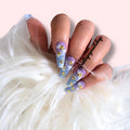 Twilight press‑on nails by CutiePop Nail Shop featuring medium‑length almond-shaped nails in a gradient blend of deep midnight blue fading into dusty purple or black. Accented with silver metallic star motifs, tiny moon charms, and scattered holographic shimmer, finished with a high-gloss gel polish. The set includes ten reusable nails, jelly adhesive tabs, a mini nail file, and a cuticle stick—designed for a dreamy, celestial manicure evoking twilit magic.