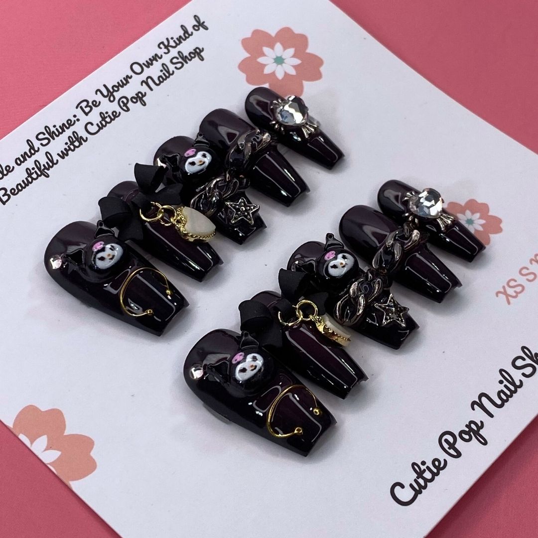 Kuromicore press on nails by CutiePop Nail Shop inspired by Kuromi, featuring medium coffin shaped nails in black and pink tones with cute gothic elements like hearts, skulls, and bows for a playful yet edgy look.


