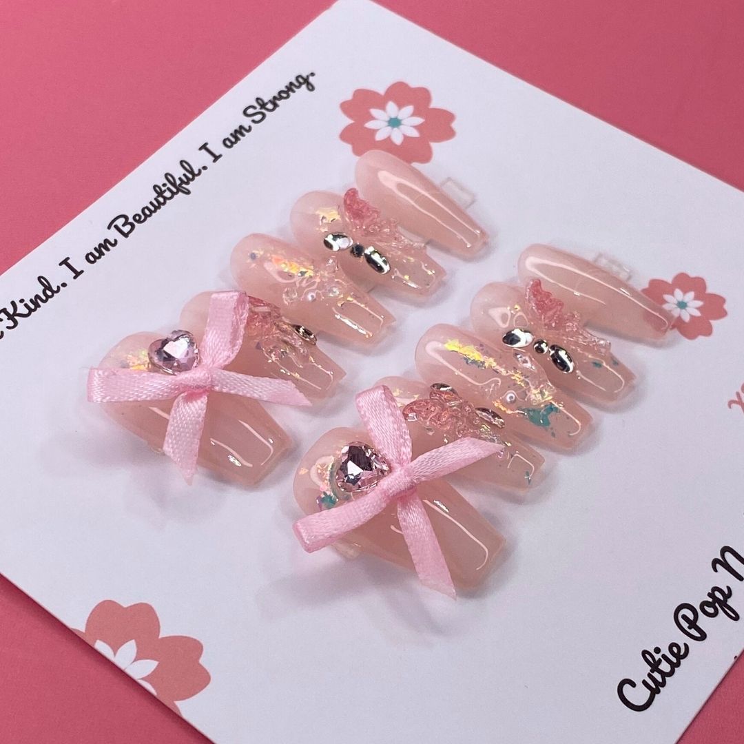 Lovely Butterfly press on nails by CutiePop Nail Shop featuring medium coffin shaped nails with a soft pastel base, adorned with a large 3D butterfly charm and delicate ribbon accents—designed for a dreamy and feminine look.

