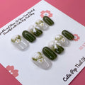 Lovely Olive press on nails by CutiePop Nail Shop featuring short round shaped nails in a soft white and olive green color palette. Adorned with delicate ornaments and charming ribbon accents, this design offers a sweet, festive-inspired look with a clean and elegant finish.

