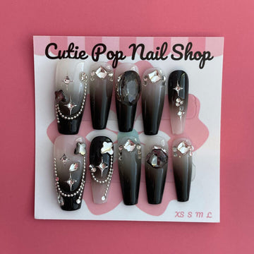 Midnight Whisper press-on nails by CutiePop Nail Shop featuring medium-length coffin-shaped nails with a deep black base, silvery metallic swirl motifs, and star-like shimmer accents. Designed in a limited-edition celestial gothic style, this set captures whispery galaxy vibes with an elegant, mysterious flair. Each kit includes 10 reusable handmade nails, jelly adhesive tabs, a mini nail file, and a cuticle stick for easy DIY application.

