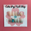 Pastel Gem press‑on nails by CutiePop Nail Shop featuring short, square-shaped nails in soft pastel hues—including blush pinks, mint green, and lavender—adorned with oversized iridescent gem embellishments and subtle metallic accents. Includes a reusable set with adhesive tabs, a mini nail file, and a cuticle stick, offering a sweet, dreamy manicure with a touch of luxe sparkle.