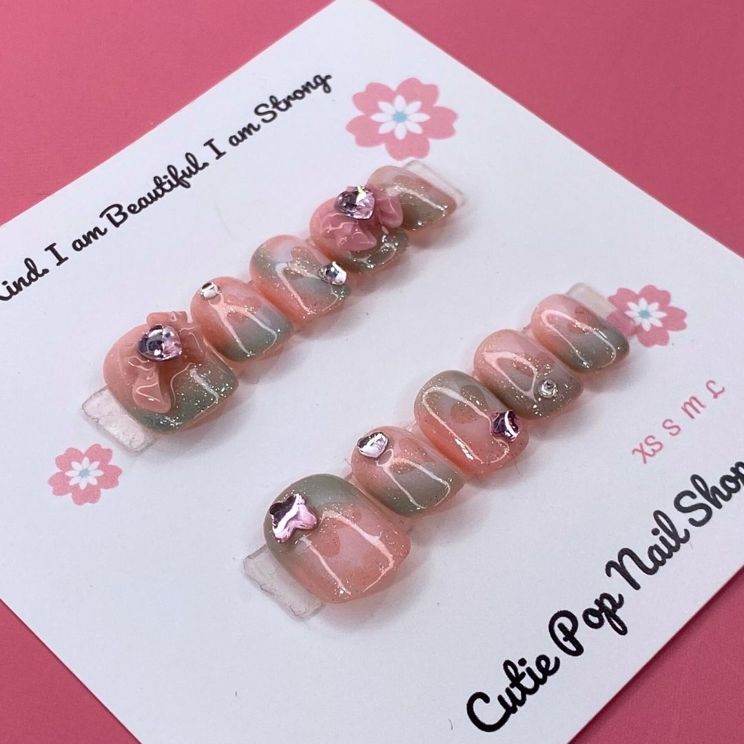 Peach Princess press on nails by CutiePop Nail Shop featuring short squoval shaped nails in soft peach tones with floral details, pearls, and subtle glitter for a sweet and elegant princess-inspired look.


