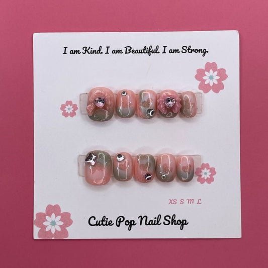 Peach Princess press on nails by CutiePop Nail Shop featuring short squoval shaped nails in soft peach tones with floral details, pearls, and subtle glitter for a sweet and elegant princess-inspired look.

