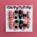 Pink Loli press on nails by CutiePop Nail Shop featuring a playful mix of pink based nails with edgy black line detailing and black accent nails adorned with ribbon, butterfly-like shapes, and heart motifs. Designed in a coffin shape, this set blends sweet and dark elements for a bold, kawaii-meets-gothic aesthetic.

