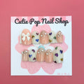 Rainbow Hearts press‑on nails by CutiePop Nail Shop featuring medium‑length round-shaped nails in a soft translucent pastel base, each adorned with hand-painted rainbow-colored heart motifs against a dreamy glossy finish. The nails come as a reusable kit—including ten handmade nails, jelly adhesive tabs, a mini nail file, and a cuticle stick—perfect for a playful yet elegant kaleidoscopic manicure.