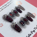 Rebel Chic press‑on nails by CutiePop Nail Shop featuring a medium‑length coffin-shaped set combining glossy jet-black, deep blood-red, and transparent nails accented with edgy skull motifs, mirrored stone embellishments, and stylized cross details—hand-painted and hand-sculpted for a bold, gothic-rock aesthetic.