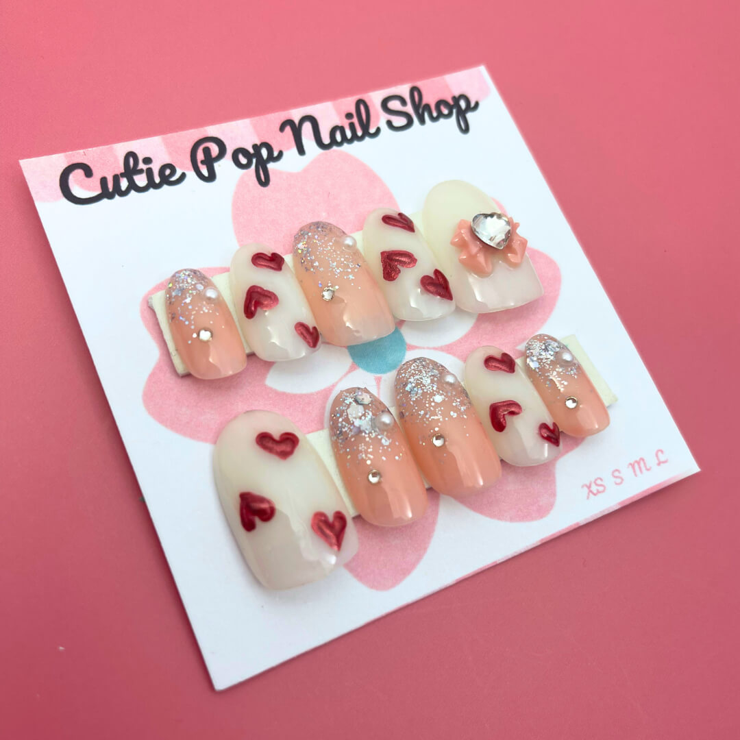 Red Hearts press-on nails by CutiePop Nail Shop featuring medium-length round-shaped nails in a bold red hue, adorned with charming red heart accents for a sweet, romantic look—perfect for Valentine’s vibes or year-round love.

