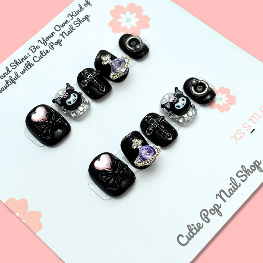 Short Kuromi press-on nails in a compact length with a soft color base, featuring 3D Kuromi character charms and cute kawaii-style accents, finished with a glossy shine – displayed on a Cutie Pop Nail Shop card.