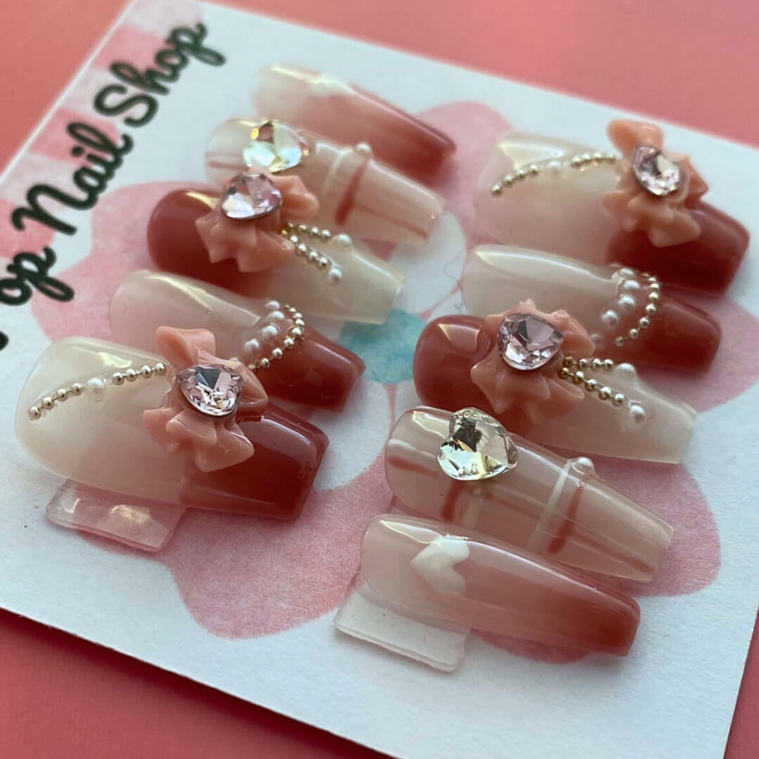 Soft Girly press‑on nails by CutiePop Nail Shop featuring medium-length coffin-shaped nails in a delicate blush pink tone with dainty rose-gold metallic accents, glitter gradient tips, and tiny bow motifs on accent nails. The kit includes 10 reusable handmade press-ons, jelly adhesive tabs, a mini nail file, and a cuticle stick—offering a soft, feminine, and elegant everyday look.