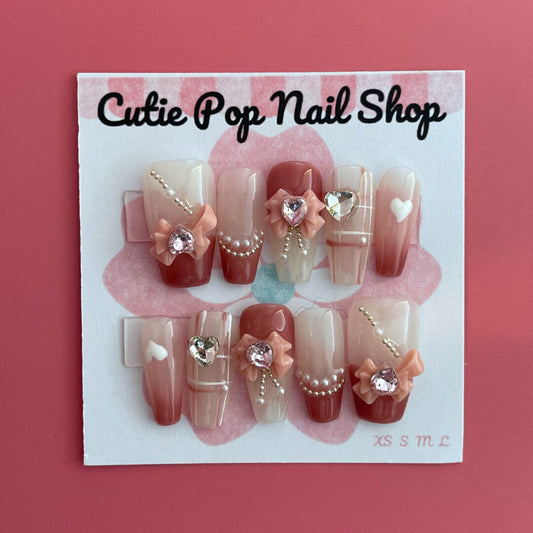 Soft Girly press‑on nails by CutiePop Nail Shop featuring medium-length coffin-shaped nails in a delicate blush pink tone with dainty rose-gold metallic accents, glitter gradient tips, and tiny bow motifs on accent nails. The kit includes 10 reusable handmade press-ons, jelly adhesive tabs, a mini nail file, and a cuticle stick—offering a soft, feminine, and elegant everyday look.