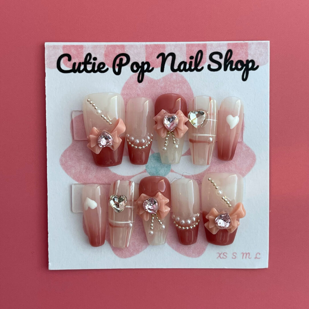 Soft Girly press‑on nails by CutiePop Nail Shop featuring medium-length coffin-shaped nails in a delicate blush pink tone with dainty rose-gold metallic accents, glitter gradient tips, and tiny bow motifs on accent nails. The kit includes 10 reusable handmade press-ons, jelly adhesive tabs, a mini nail file, and a cuticle stick—offering a soft, feminine, and elegant everyday look.