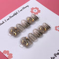 Soft Goth press-on nails by CutiePop Nail Shop featuring short squoval-shaped nails in black and muted tones. Designed with delicate gothic accents like lace patterns, hearts, and subtle cross motifs for a chic, edgy, and softly mysterious look.

