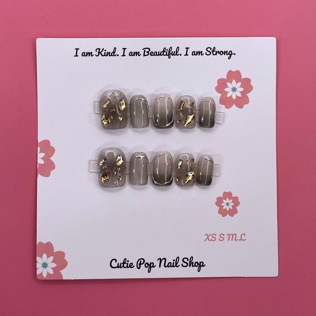 Soft Goth press-on nails by CutiePop Nail Shop featuring short squoval-shaped nails in black and muted tones. Designed with delicate gothic accents like lace patterns, hearts, and subtle cross motifs for a chic, edgy, and softly mysterious look.


