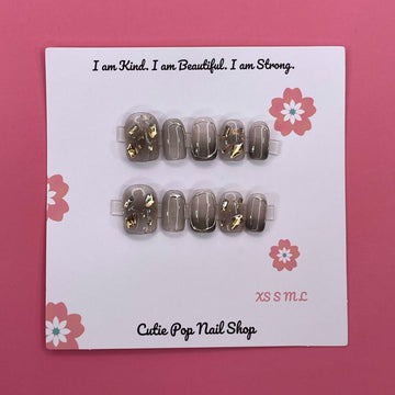 Soft Goth press-on nails by CutiePop Nail Shop featuring short squoval-shaped nails in black and muted tones. Designed with delicate gothic accents like lace patterns, hearts, and subtle cross motifs for a chic, edgy, and softly mysterious look.


