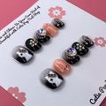 Spooky Sparkle press-on nails by CutiePop Nail Shop featuring short square-shaped nails in a Halloween-inspired black and purple palette. Decorated with glitter, shimmer details, and cute spooky accents like black cats and ghostly elements, these nails add a fun, festive twist to your October look. Comes as a reusable kit with 10 handmade nails, jelly adhesive tabs, a mini nail file, and a cuticle stick for easy, mess-free application.