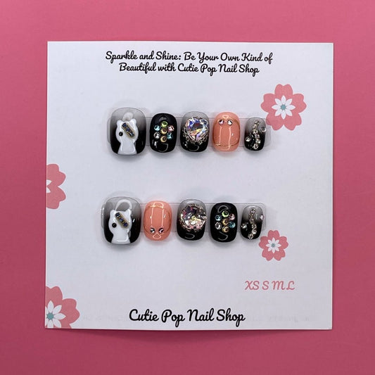 Spooky Sparkle press-on nails by CutiePop Nail Shop featuring short square-shaped nails in a Halloween-inspired black and purple palette. Decorated with glitter, shimmer details, and cute spooky accents like black cats and ghostly elements, these nails add a fun, festive twist to your October look. Comes as a reusable kit with 10 handmade nails, jelly adhesive tabs, a mini nail file, and a cuticle stick for easy, mess-free application.