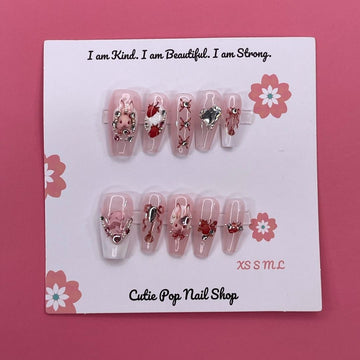Strawberry Bunny press-on nails by CutiePop Nail Shop featuring medium-length coffin-shaped nails in soft pink tones with adorable strawberry and bunny designs. Accented with tiny bows, pearls, and glossy details for a sweet, kawaii-inspired aesthetic.

