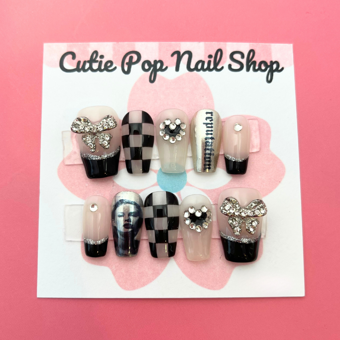 taylor swift inspired fake nails with checkered pattern and black french tip with bow on the thumb. The words "reputation" on a silver chrome nail, and taylor swift's face on another chrome nail. 