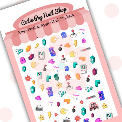 This image showcases Cutie Pop Nail Shop’s RetroGamer nail decals against a white background with a Cutie Pop Nail Shop logo and watermark. These nail decal designs include vintage video game controllers, block puzzles, power-up stars, lightning bolts, arcade machines, handheld gaming devices, red, yellow, and green gems, bombs with lit fuses, health bars, animated ghosts, and yellow circles with messing segments (to resemble a mouth) eating yellow dots.